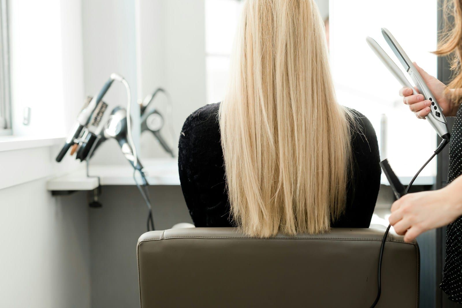 Keratin za kosu u Kragujevcu, ilustracija: duga ravna svetla kosa u stolici, a frizerka sa strane drži presu